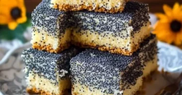 Eine Scheibe Mohnkuchen auf einem Teller mit einer Tasse Kaffee im Hintergrund.