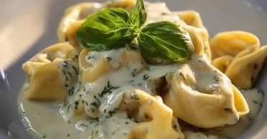 Tortellini mit Kräuter-Käse-Sauce auf einem Teller serviert.