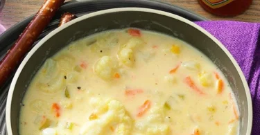 Schüssel mit cremiger Blumenkohlsuppe, garniert mit frischen Kräutern.