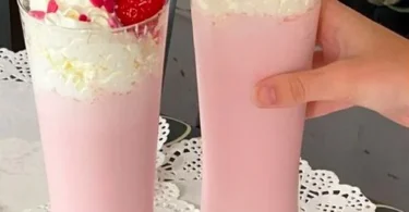Frischer Erdbeer-Milchshake in einem Glas mit Erdbeeren und Sahne verziert