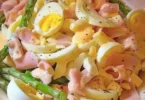 Spargelsalat mit Schinken und Ei auf einem Teller angerichtet.