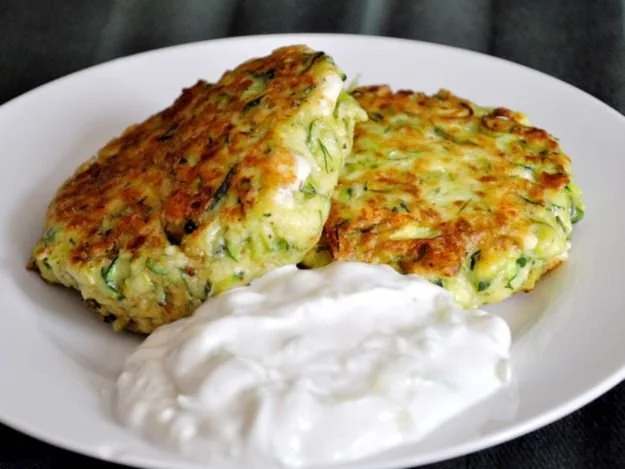 Zucchini-Feta-Patties mit Tzatziki auf einem Teller