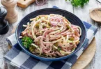 Leckerer Wurst- und Käse-Salat auf einem Teller, dekoriert mit frischen Kräutern.