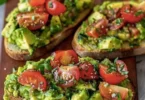 Avocadobrot mit frischen Tomaten auf einer Holztafel serviert.