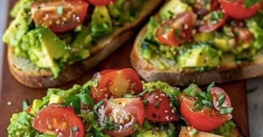 Avocadobrot mit frischen Tomaten auf einer Holztafel serviert.