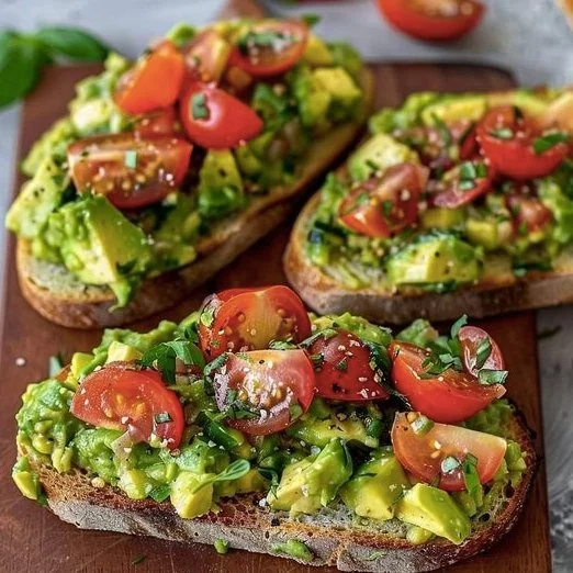Avocadobrot mit frischen Tomaten auf einer Holztafel serviert.