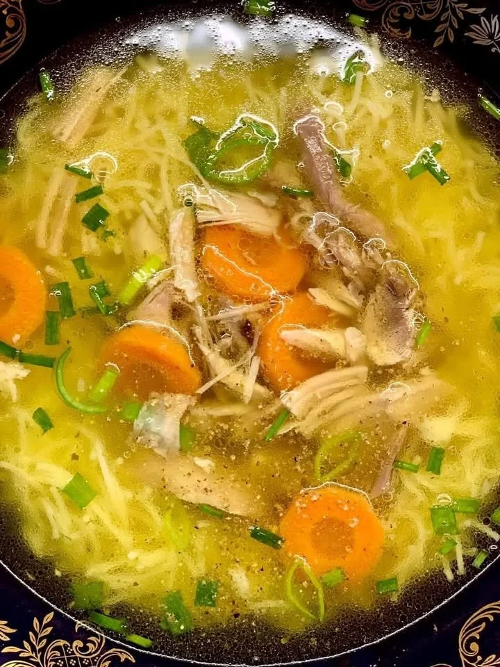 Schüssel mit dampfender Hühnersuppe, garniert mit frischen Kräutern