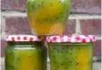 Glas mit Mango-Kiwi-Marmelade auf einem Holzbrett