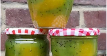 Glas mit Mango-Kiwi-Marmelade auf einem Holzbrett