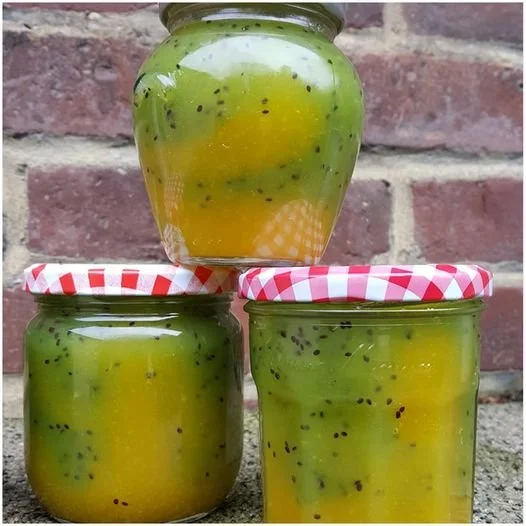 Glas mit Mango-Kiwi-Marmelade auf einem Holzbrett