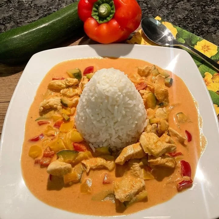 Paprika-Zucchini-Sahne Hähnchen mit Reis auf einem Teller serviert
