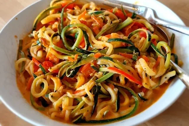 Zucchini-Spaghetti mit frischen Zutaten auf einem Teller serviert